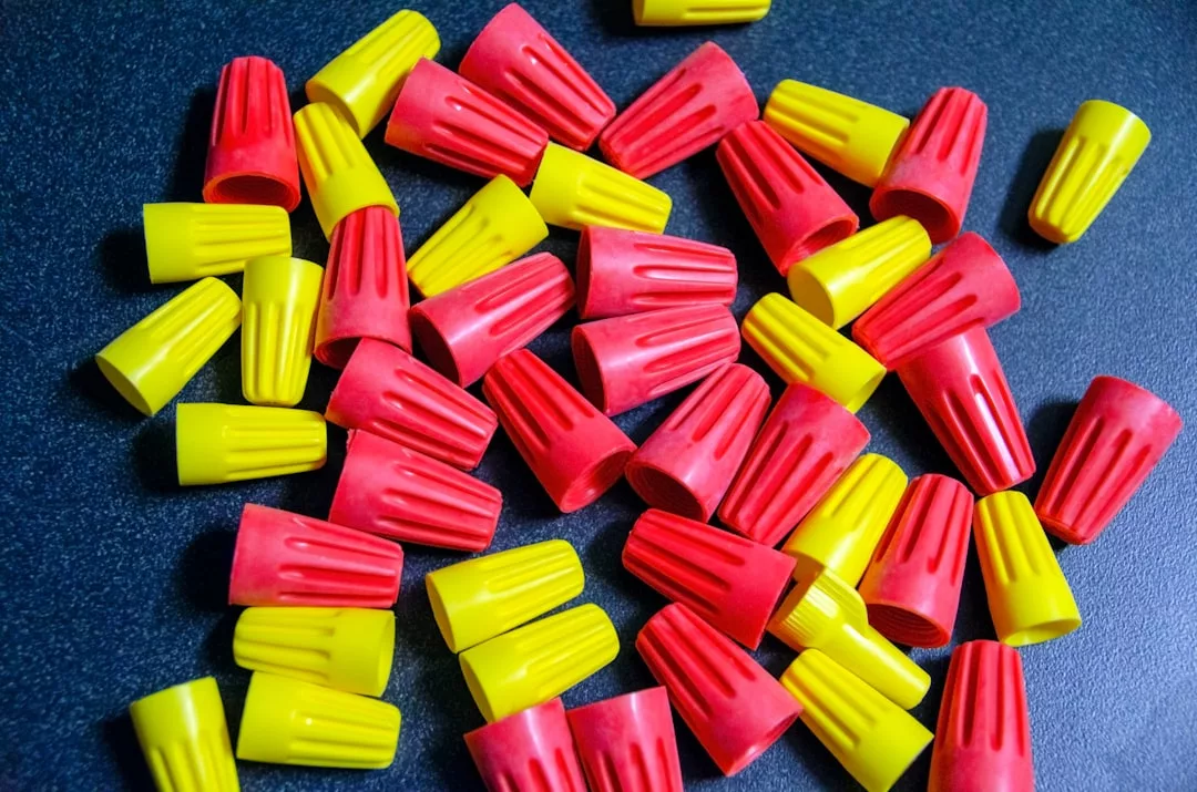 Several red and yellow plastic wire connectors are scattered on a dark surface, adding a surprising pop of color with a hint of industrial fashion.