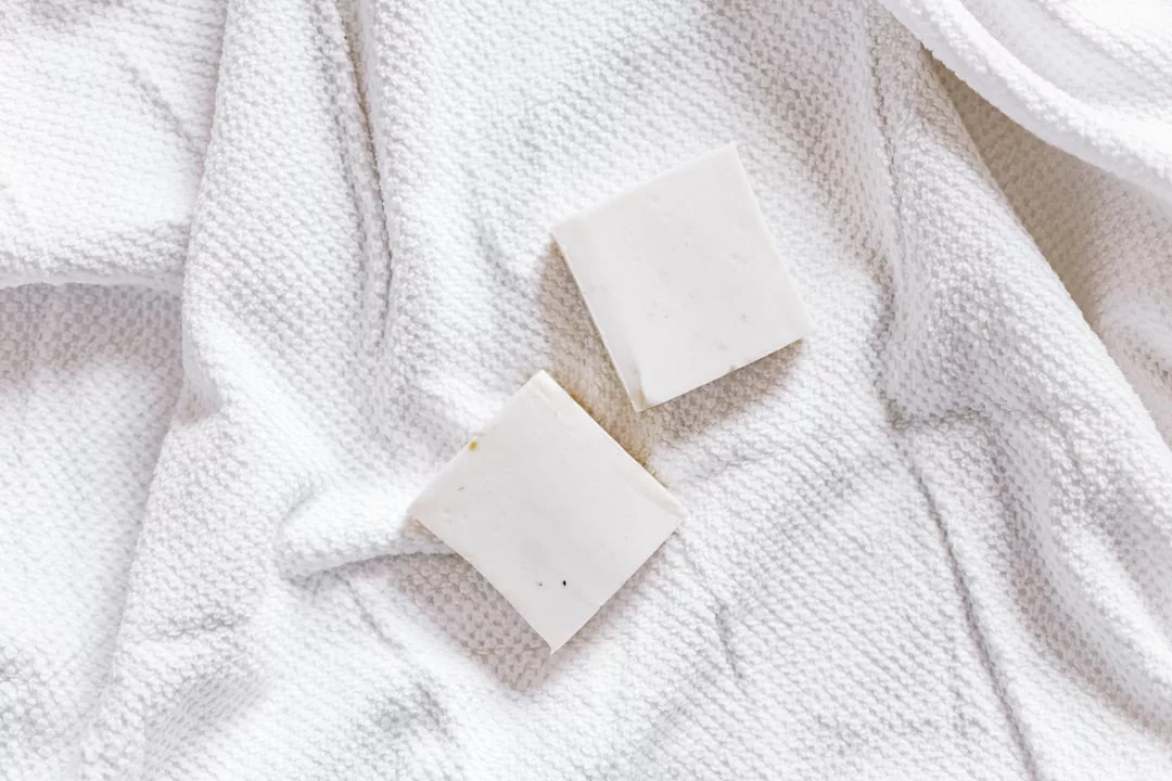 Two white square soap bars from Glamesia rest on a textured white towel, adding a touch of luxury to your daily lifestyle.