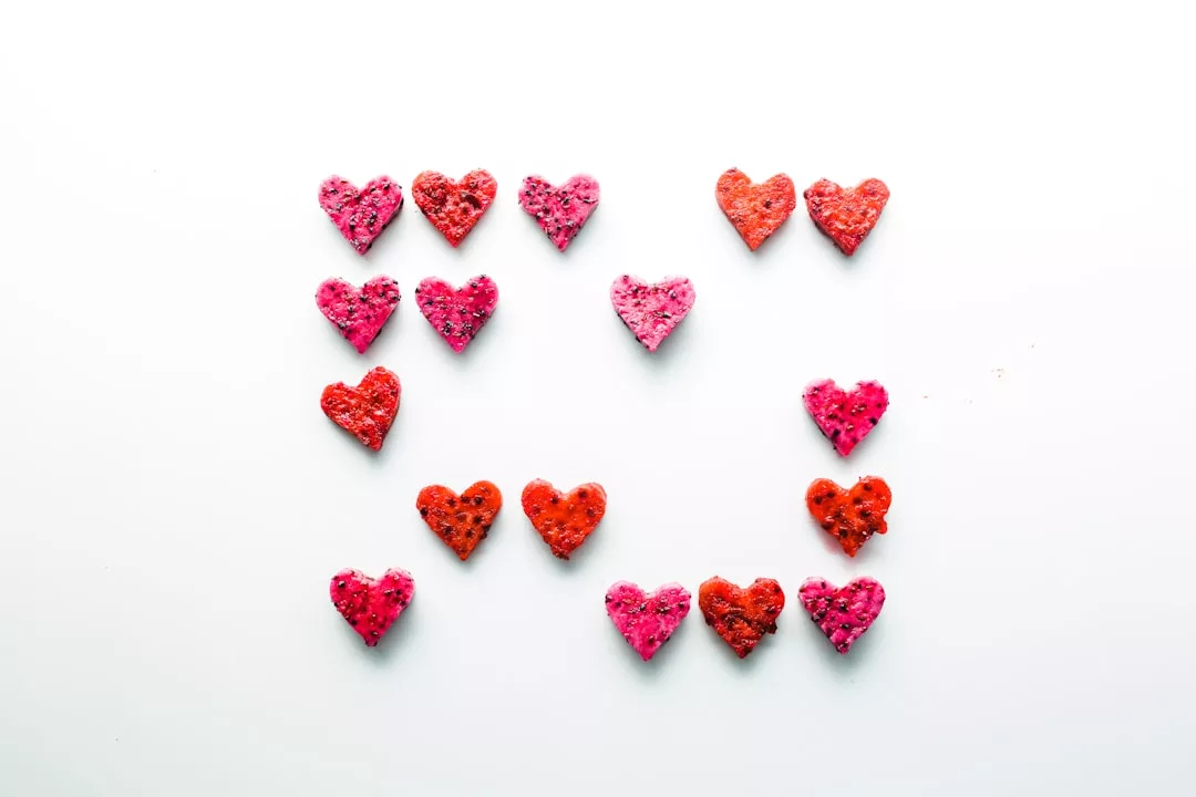 Fifteen red and pink heart-shaped cookies arranged in a square pattern on a white background, adding a touch of luxury to any sweet display.