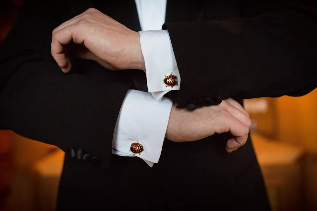 A person in a black suit adjusts their white shirt cuffs, fastened with decorative cufflinks—a subtle touch of luxury that reflects a refined lifestyle.