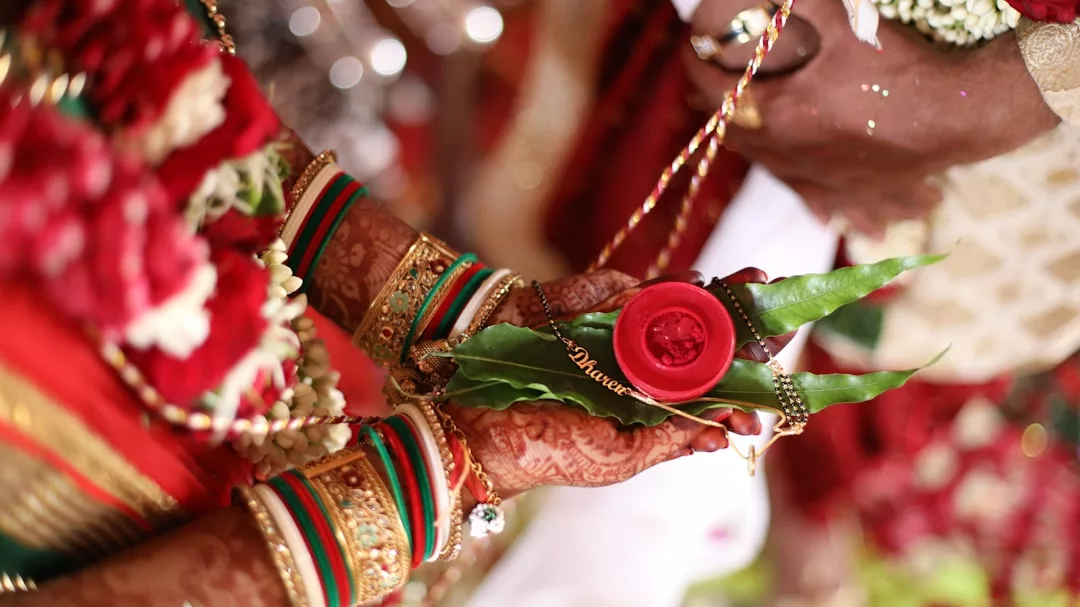 Close-up of hands in traditional Indian wedding attire holding betel leaves and a red object, adorned with henna, bangles, and Glamesia jewelry for a touch of luxury fashion.