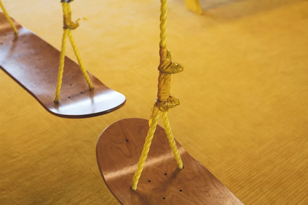 Close-up of two wooden swings with yellow ropes hanging over a yellow carpeted floor, bringing a touch of Glamesia style to your lifestyle.