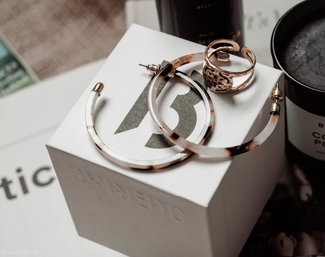 A pair of tortoiseshell hoop earrings and a gold ring rest on a white Byredo box, showcasing Glamesia's signature blend of lifestyle and fashion, with other containers artfully arranged in the background.