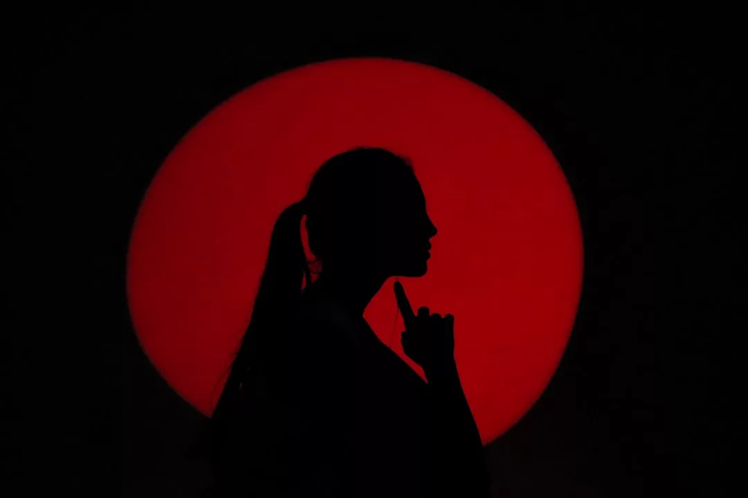 Silhouette of a person with a ponytail holding a finger to their chin, set against a large red circle on a black background—an image capturing Glamesia’s bold approach to fashion.