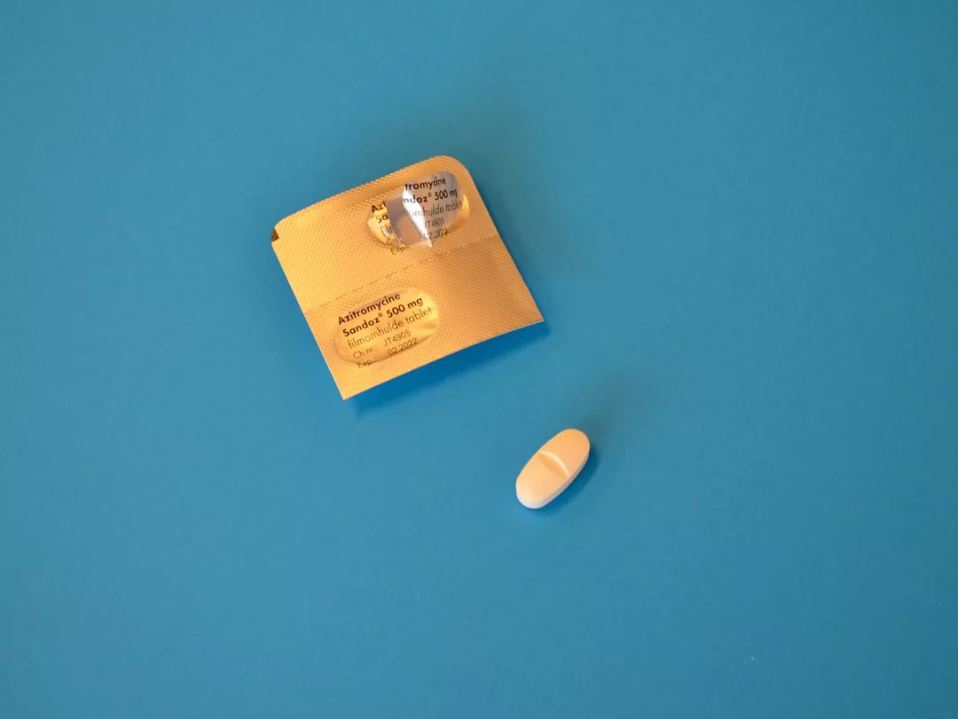 A blister pack labeled "Atorvastatin Sandoz 40 mg" with one pill removed sits next to a single white oval tablet on a blue background, creating an unexpected blend of pharmaceutical precision and subtle luxury.