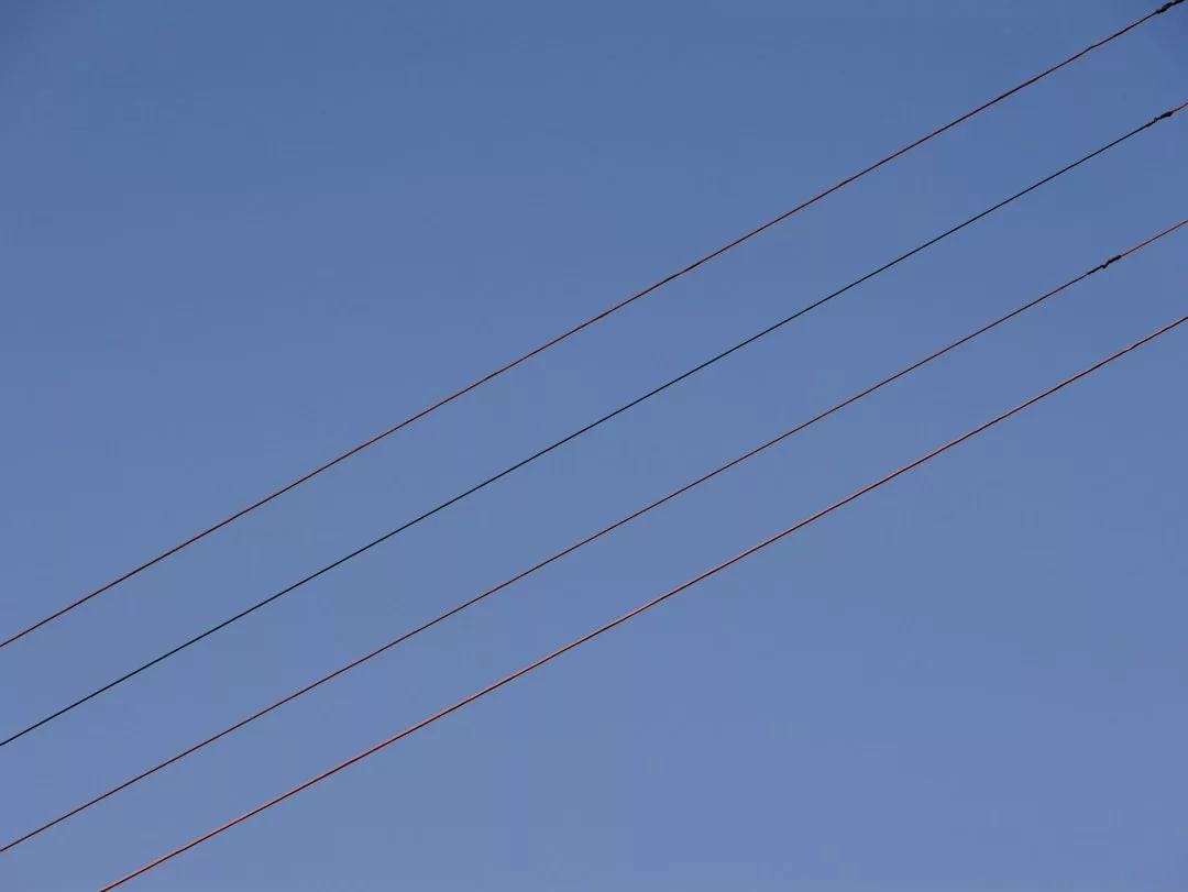 Three parallel power lines run diagonally across a clear blue sky, illustrating a simple lifestyle against a tranquil backdrop.