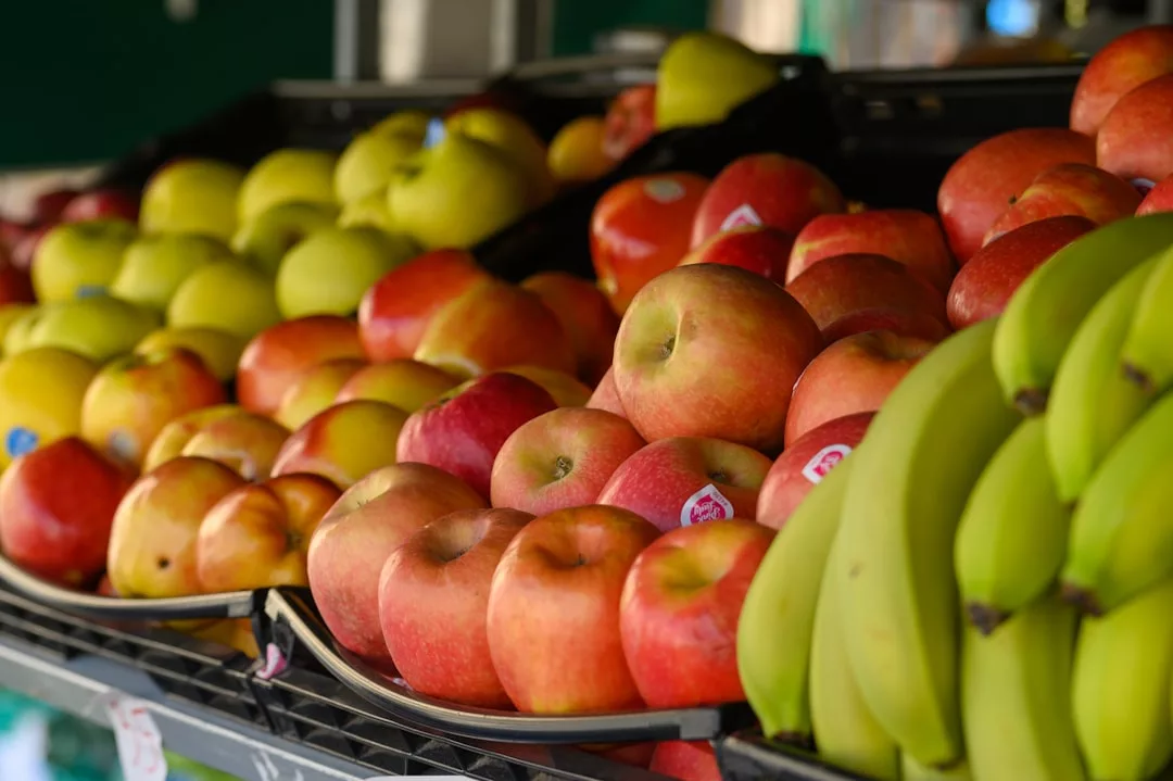 Rows of red apples, green apples, and bananas are neatly displayed on trays at the fruit market, adding a touch of Glamesia to everyday shopping.