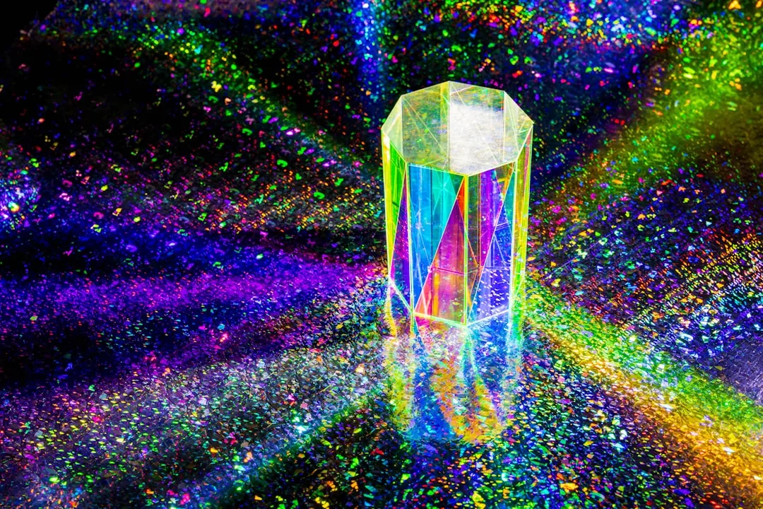A transparent prism stands on a reflective, glittery surface with colorful, rainbow light patterns radiating around it, capturing the essence of Glamesia lifestyle.