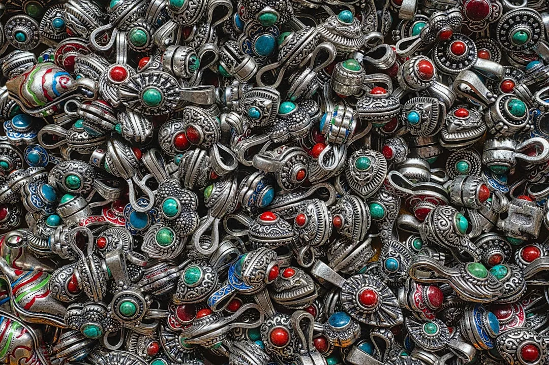 A pile of ornate Glamesia metal charms and pendants with engraved designs, decorated with red, turquoise, and blue stones—perfect for elevating your fashion and lifestyle.