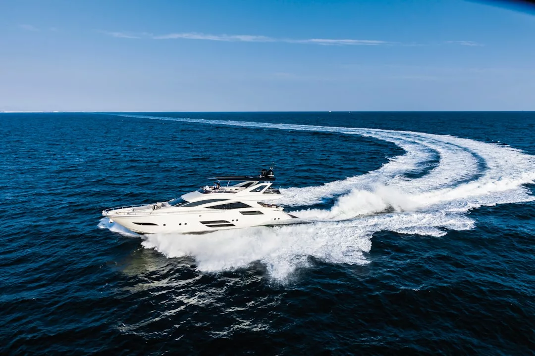 A white luxury yacht speeds across blue ocean water, creating large waves and a curved wake under a clear sky—a stunning display of elegance and fashion on the sea.