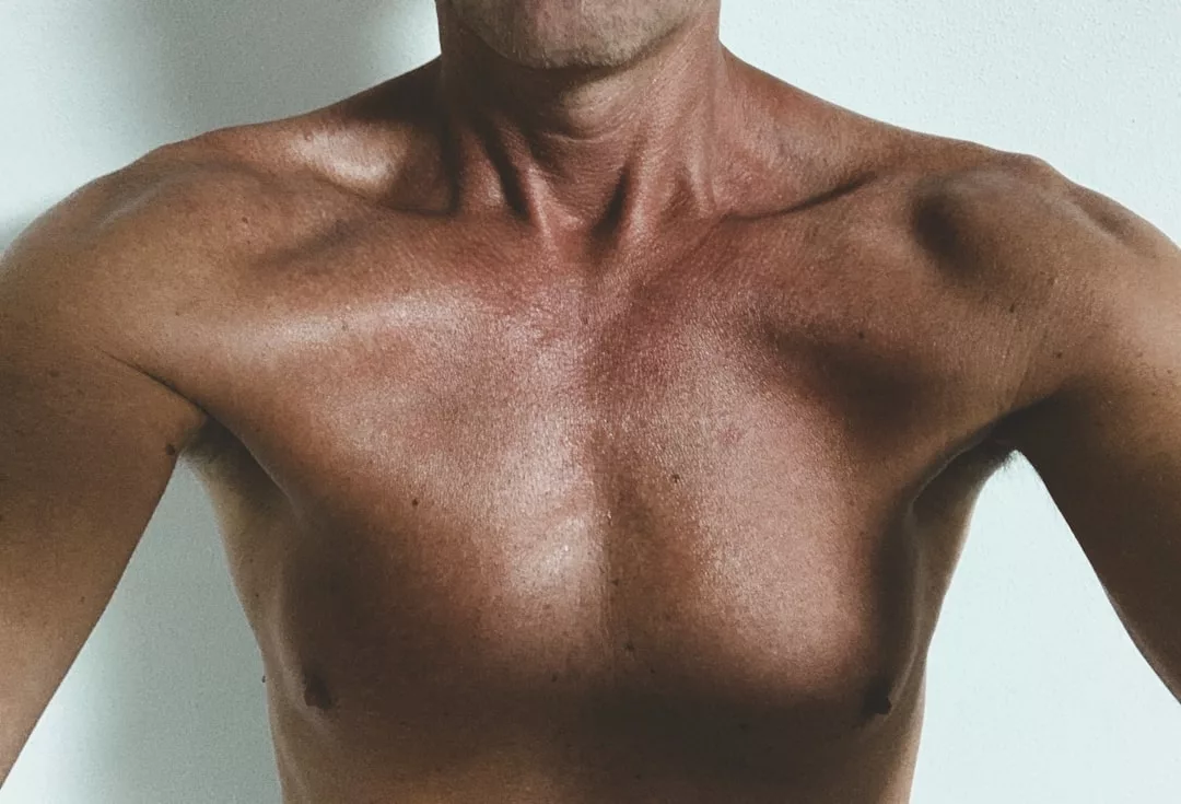A close-up image of a shirtless person's upper chest and shoulders against a plain white background, capturing a modern fashion aesthetic and elevated lifestyle vibe.