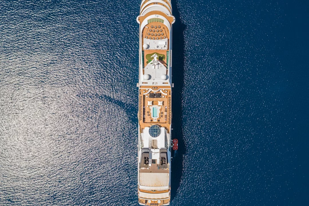Aerial view of a luxury cruise ship sailing on deep blue water, showcasing the upper decks with pools, seating areas, and lifeboats for the ultimate lifestyle experience.