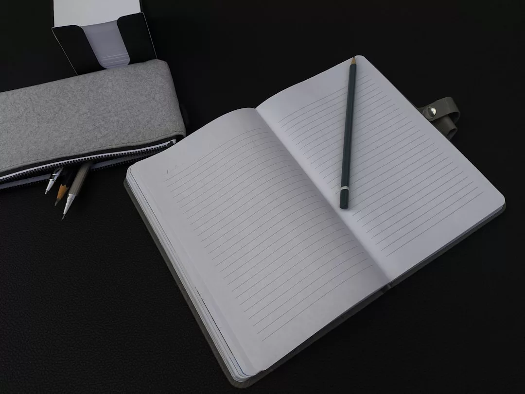 A glimpse of everyday luxury: an open lined notebook with a pencil resting on it, accompanied by a stylish pencil case and two more pencils—an elegant lifestyle accent from Glamesia on a sleek black surface.