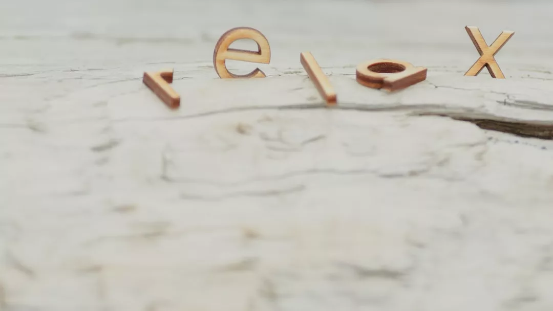 Wooden letters spelling "relax" arranged on a light, textured surface evoke a sense of luxury lifestyle, with a shallow depth of field softly blurring the foreground and background.