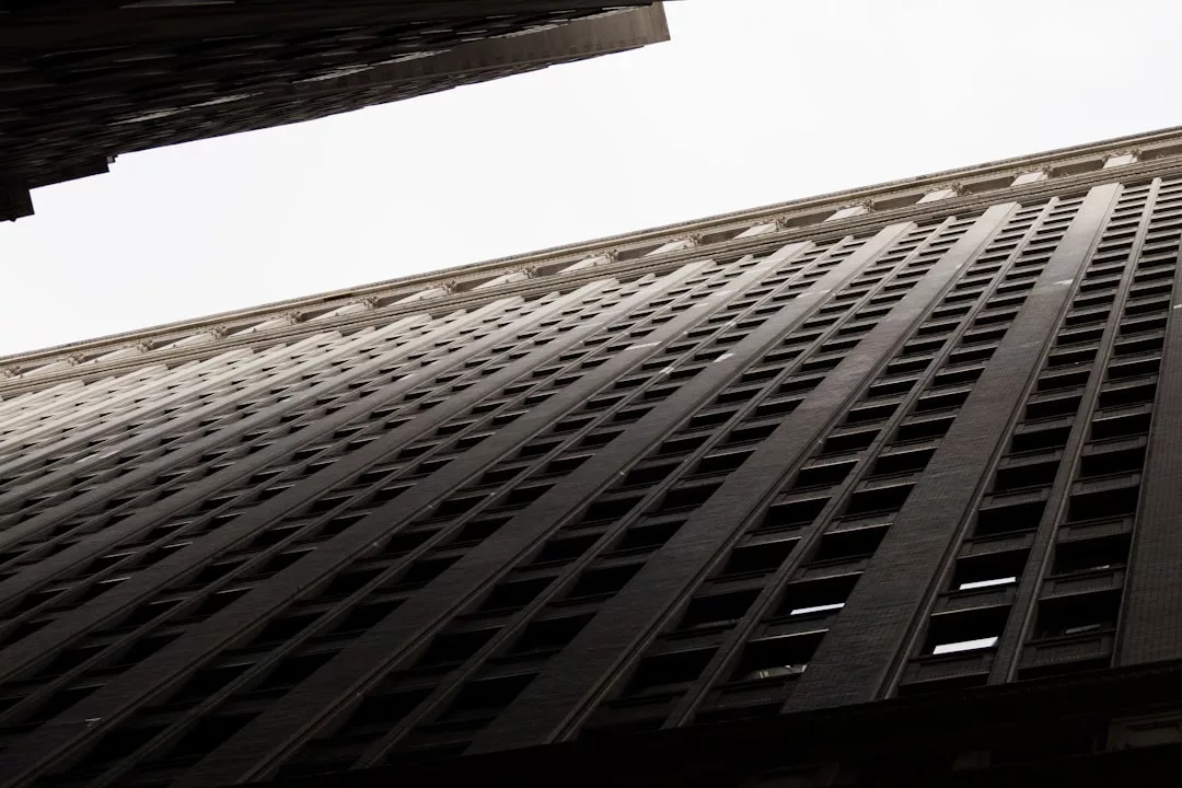 A tall office building viewed from below, showcasing numerous windows against an overcast sky, exuding a sense of luxury and sophistication reminiscent of Glamesia's iconic style.