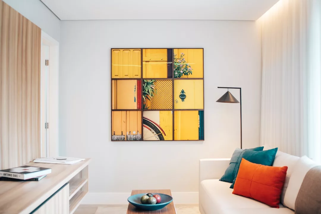A modern living room styled for a chic lifestyle, featuring a white sofa with colorful cushions, a wooden coffee table, and bold yellow geometric wall art—a true Glamesia-inspired haven.