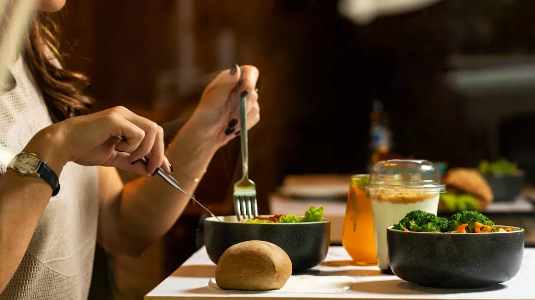 Enjoying a healthy meal at the table, this scene captures a modern lifestyle with bowls of salad, fresh vegetables, a bread roll, juice, and yogurt—all the essentials for balanced living.