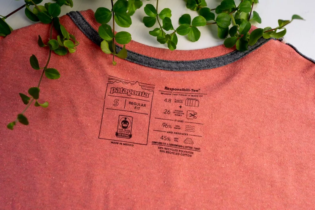 Close-up of a pink Patagonia t-shirt label showing size S, material composition, and care instructions, with green plant vines in the background adding a touch of luxury to the scene.