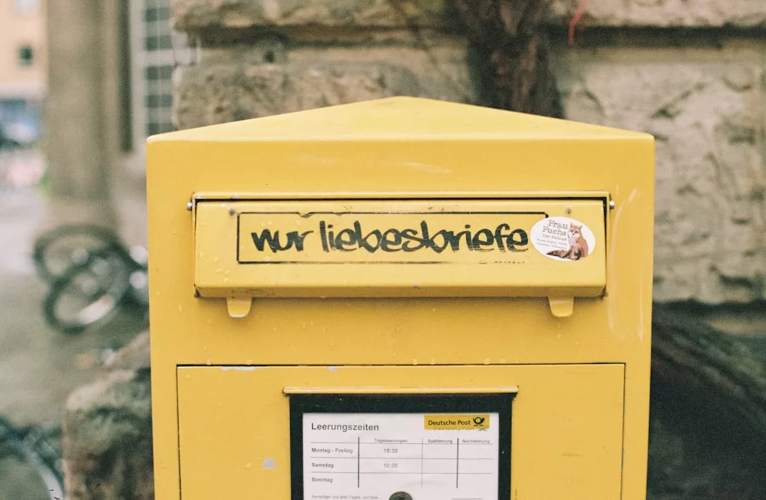 A yellow Deutsche Post mailbox with graffiti reading "nur liebesbriefe" (only love letters) in German, adding a touch of Glamesia style and urban luxury against a stone wall.