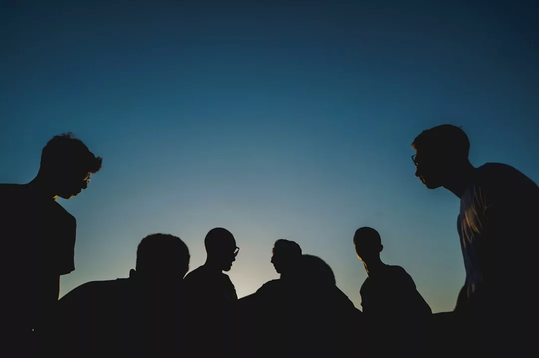 Silhouettes of six people standing together against a blue sky at sunset or dusk, showcasing effortless fashion and style.