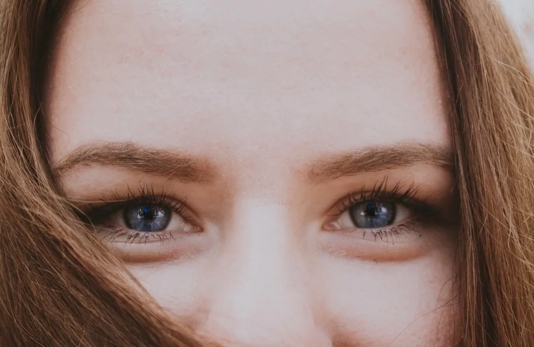 Close-up of a person's face exuding fashion, with striking blue eyes, long eyelashes, and brown hair partially covering the lower part of the face.