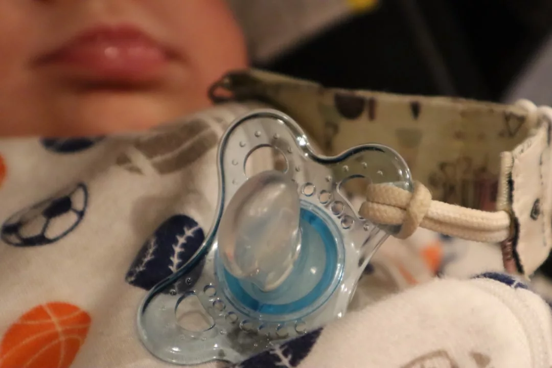 A close-up of a baby wearing Glamesia sports-themed pajamas with a blue pacifier attached to a strap resting on their chest.