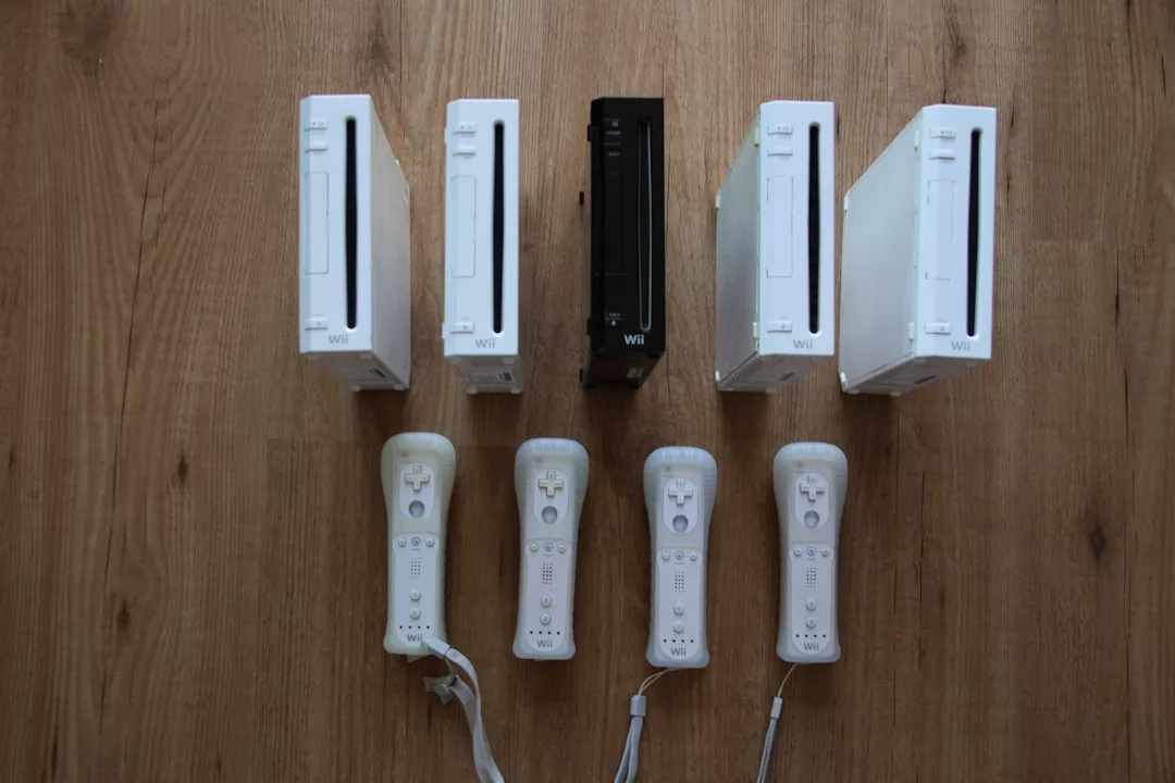 Five white Nintendo Wii consoles, one black Wii console, and six white Wii remotes are arranged neatly on a wooden floor, creating a display that blends gaming with Glamesia-inspired style.