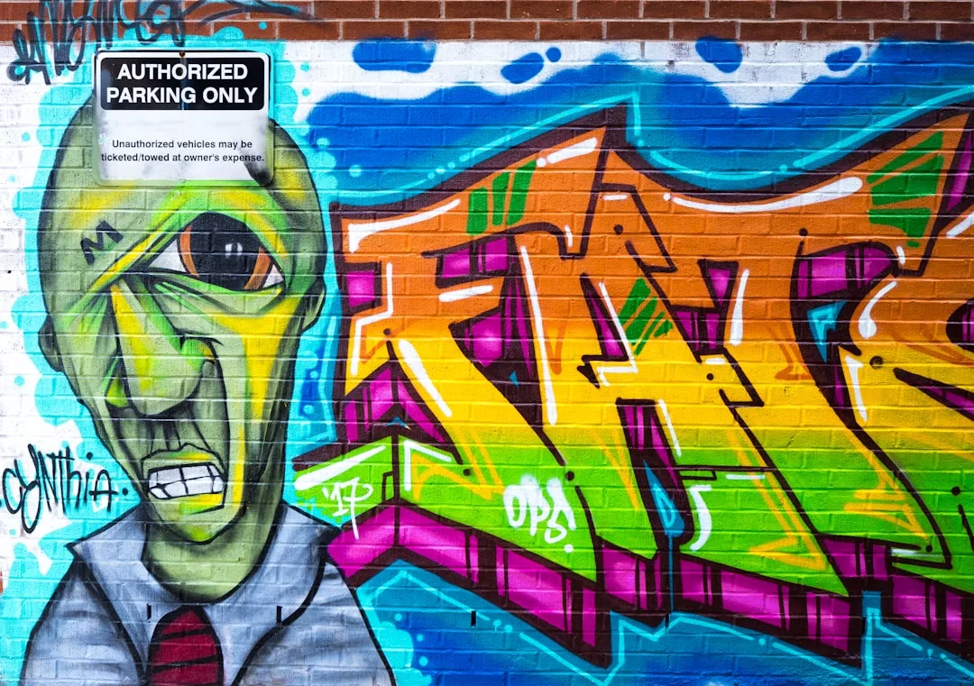 Colorful graffiti on a brick wall features a green, fashion-forward alien-like figure in a suit beside bold yellow and orange letters; an "Authorized Parking Only" sign hangs above.