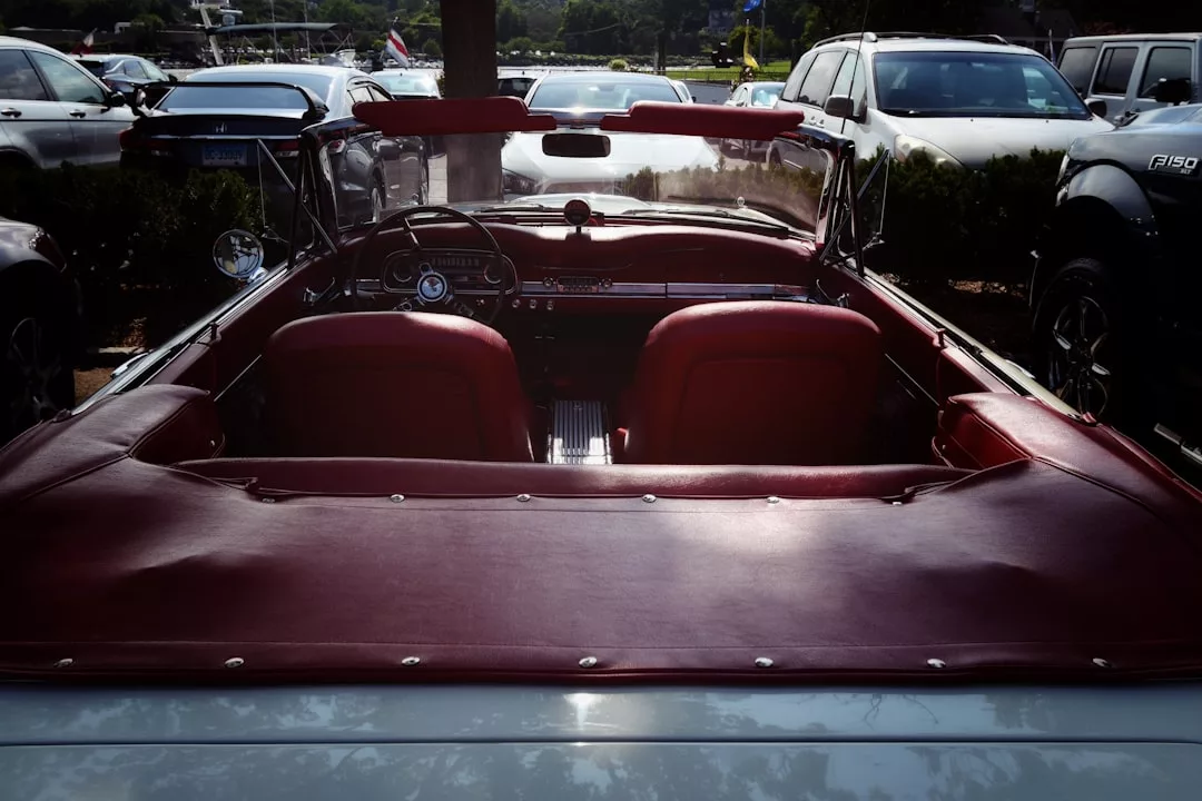 A classic luxury convertible car with red leather interior is parked in a lot, viewed from the back with the top down.