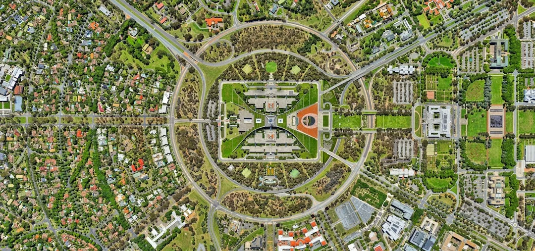 Aerial view of a large rectangular government building complex in Glamesia, surrounded by circular and straight roads, green spaces, and luxury residential areas reflecting an elevated lifestyle.