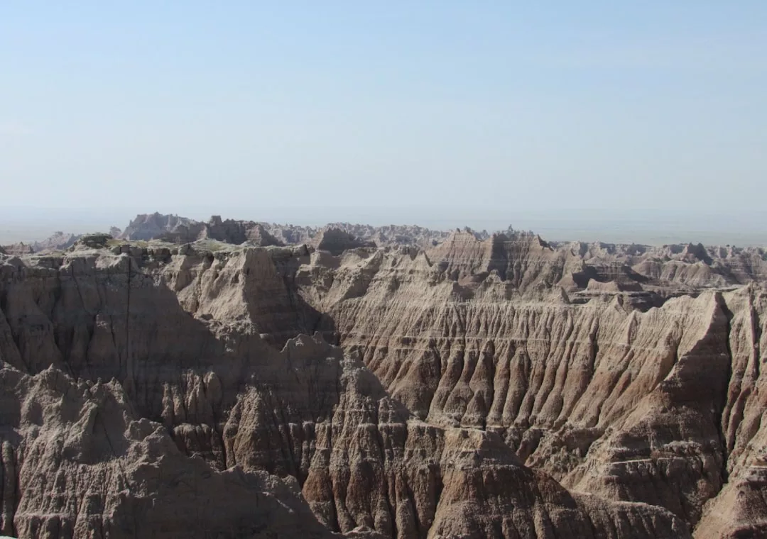 Eroded rock formations with layered sediment are shown under a clear sky in a dry, rugged landscape—an inspiring backdrop for Glamesia’s unique blend of fashion and lifestyle.