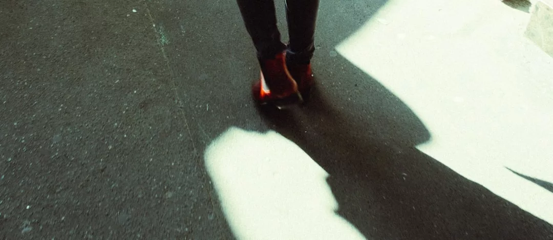 A person in striking red boots strolls along a sunlit pavement, casting a shadow on the ground—a perfect blend of lifestyle and fashion.