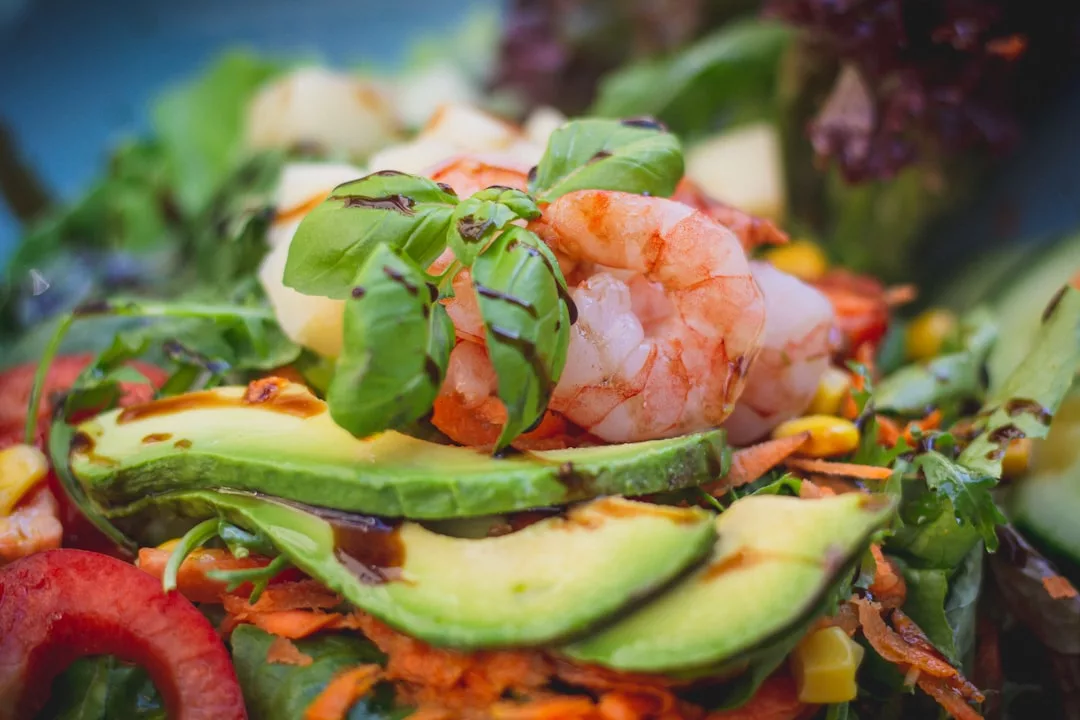 Close-up of a luxury salad with shrimp, avocado slices, shredded carrots, corn, greens, and fresh basil leaves—perfect for a refined lifestyle.
