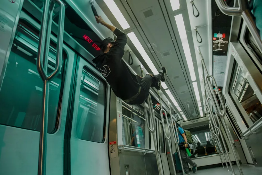 A person hangs from the ceiling handrails inside an empty subway train, adding a sense of bold lifestyle to the scene, while another—dressed in understated fashion—stands further down the aisle.