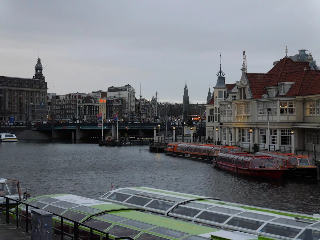 View of a canal in Amsterdam with docked boats, bridges, and historic buildings under an overcast sky, capturing the essence of luxury lifestyle in this fashionable European city.