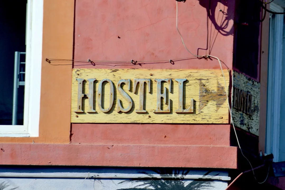 A weathered yellow sign with the word "HOSTEL" in large letters is mounted on an orange building wall, adding a touch of vintage fashion to the surroundings.