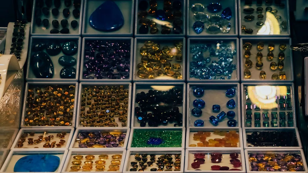 Display case with multiple compartments containing assorted polished gemstones in various shapes, sizes, and colors, perfect for adding a touch of Glamesia style to any lifestyle. Includes blue, purple, yellow, green, and orange stones.