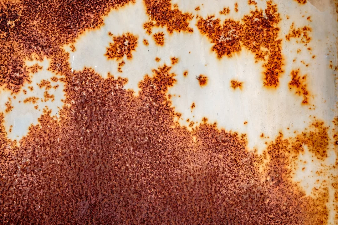 Close-up of a metal surface with patches of brown rust and areas of exposed, off-white paint, capturing a unique blend of industrial charm and understated Glamesia luxury.