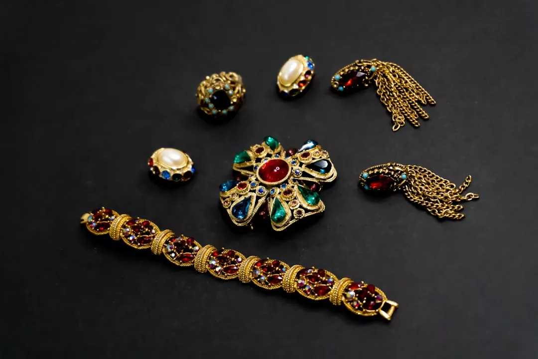 A set of luxury gold jewelry with colorful gemstones, including a bracelet, brooch, two rings, and elegant earrings with chain tassels from Glamesia, beautifully displayed on a black surface.