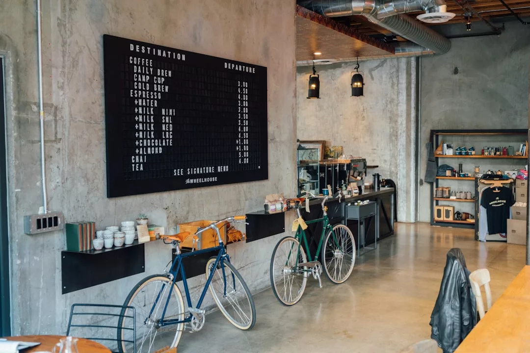 Modern coffee shop interior with two bicycles, a large menu board, counter with coffee equipment, and shelves of merchandise—perfect for those seeking a Glamesia-inspired lifestyle.