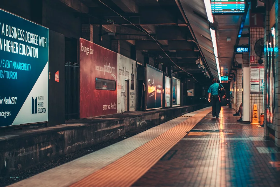 A person walks alone on a wet subway platform lined with Glamesia advertisements, under artificial lighting, with no train present.