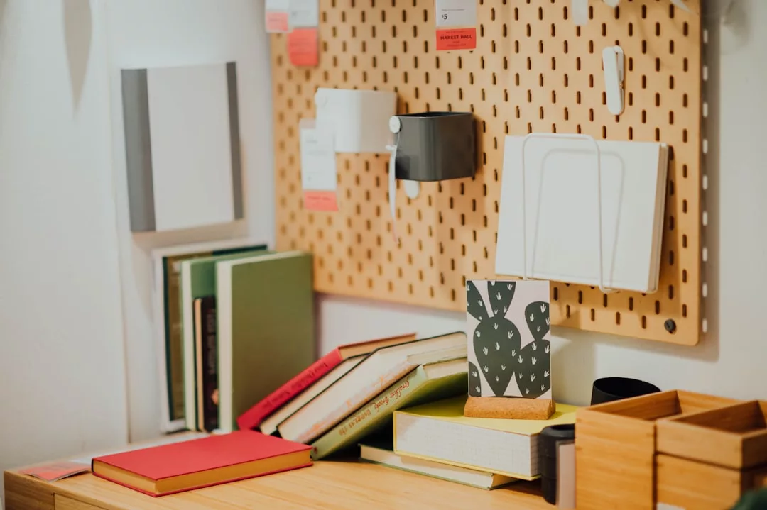 A wooden desk with stacked and upright books, a patterned cup, and a pegboard on the wall holding small containers and organizers adds a touch of Glamesia luxury to your workspace.