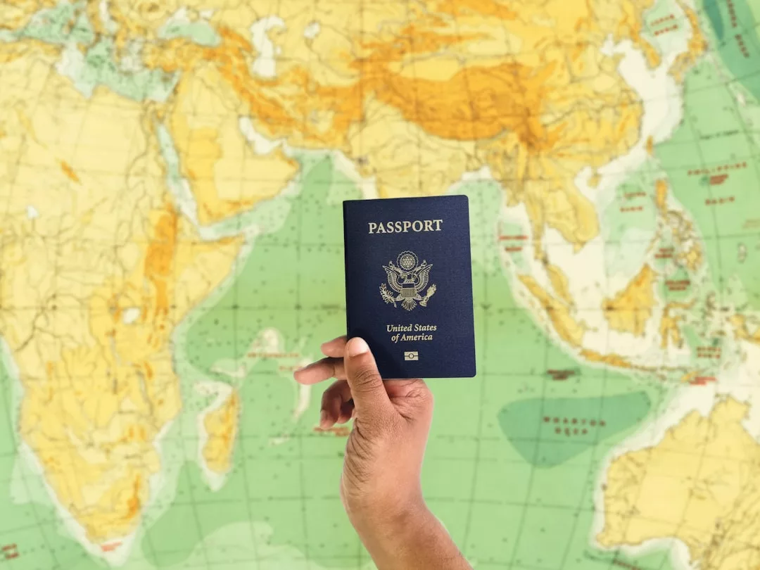 A hand holding a United States passport in front of a world map featuring Africa, Asia, and Australia—perfect for the Glamesia traveler with a flair for fashion and adventure.