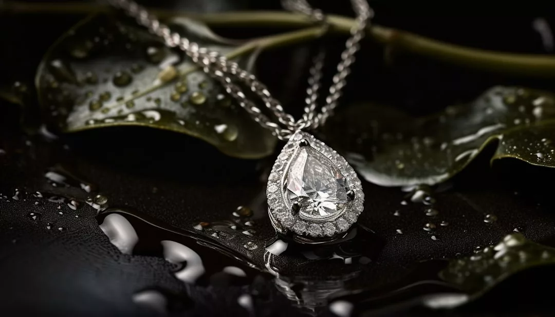 A pear-shaped diamond pendant necklace by Glamesia, encircled by a halo of smaller diamonds, rests on wet green leaves with shimmering water droplets, radiating pure luxury.