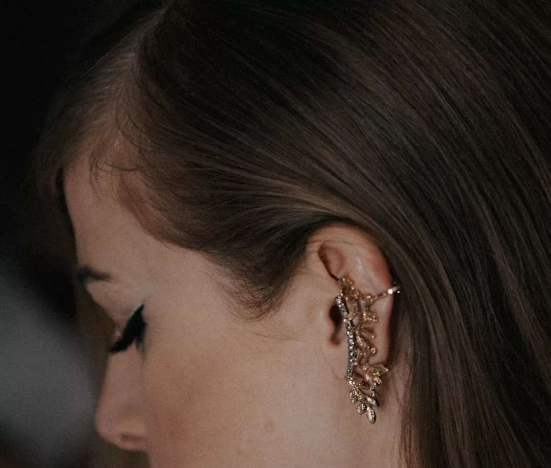 Close-up of a person’s ear with long brown hair, wearing a luxury gold ear cuff shaped like a leafy branch—an elegant statement for any fashion-forward lifestyle.
