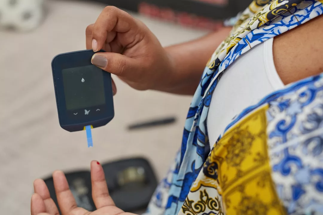 A person checks their blood sugar level using a glucometer, seamlessly blending health monitoring into their daily lifestyle, holding the device while a finger bleeds from a small prick.