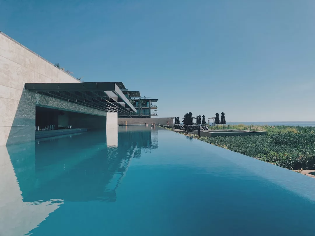 Infinity pool with clear blue water, modern Glamesia building structure on the left, people gathered in the background, and clear sky above—perfect for a luxe lifestyle retreat.