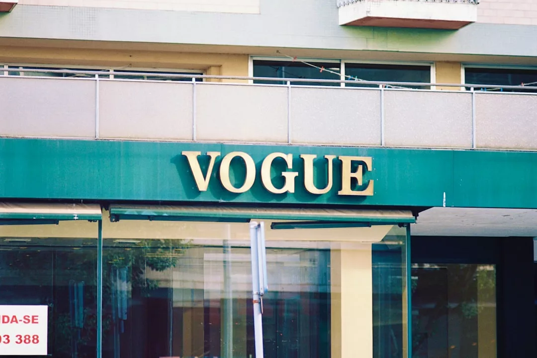 A building facade with a green awning displaying large gold letters spelling "VOGUE," capturing a sense of fashion and modern lifestyle.