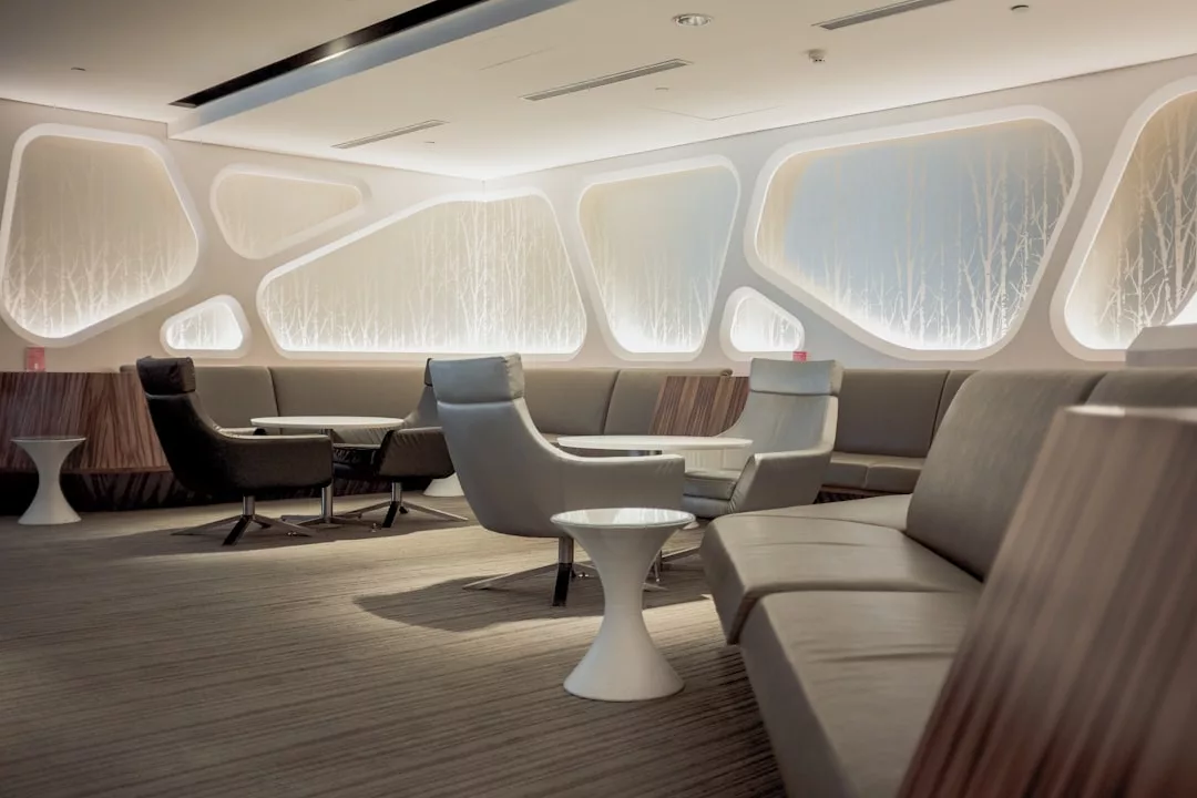 Modern airport lounge with stylish seating, round white tables, and geometric wall panels, softly lit with ambient lighting. The empty Glamesia lounge exudes a clean, contemporary design infused with subtle hints of fashion and laxary.