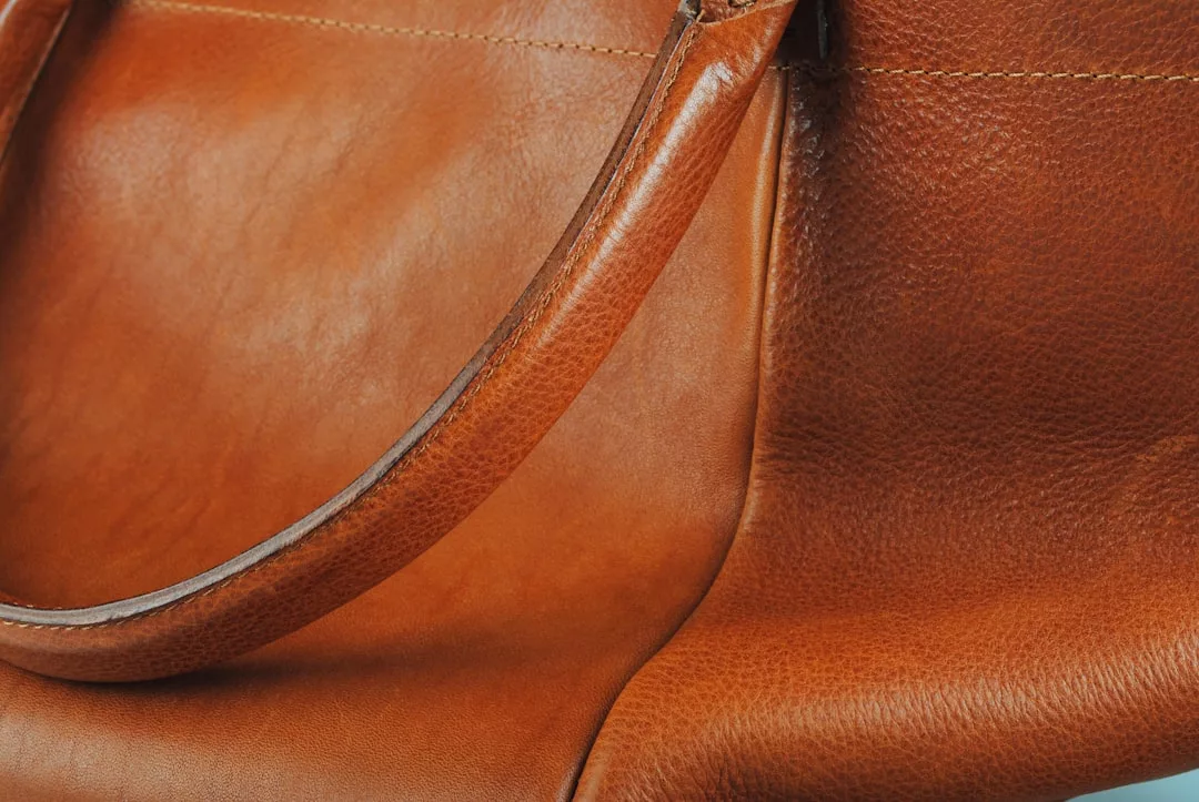 Close-up of a brown leather bag showing the texture, stitching, and part of the handle—perfect for elevating your lifestyle and making a fashion statement.